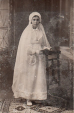 Carte-photo Communiante tenant un missel, appuyée sur un prie-dieu.