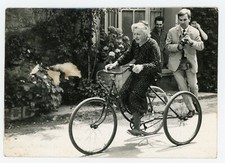 PHOTO, une femme âgée vélo ancien tricycle  suivie par homme à la caméra