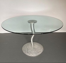 CETTE TABLE AU PLATEAU CIRCULAIRE EN DALLE DE VERRE REPOSE SUR UNE BASE ONDULÉE